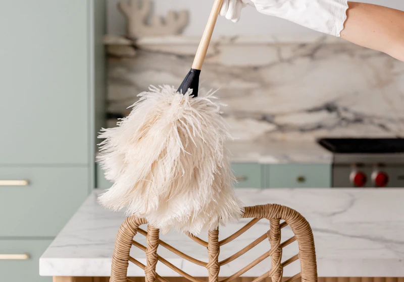 Cleaner dusting a modern home kitchen with a feather duster